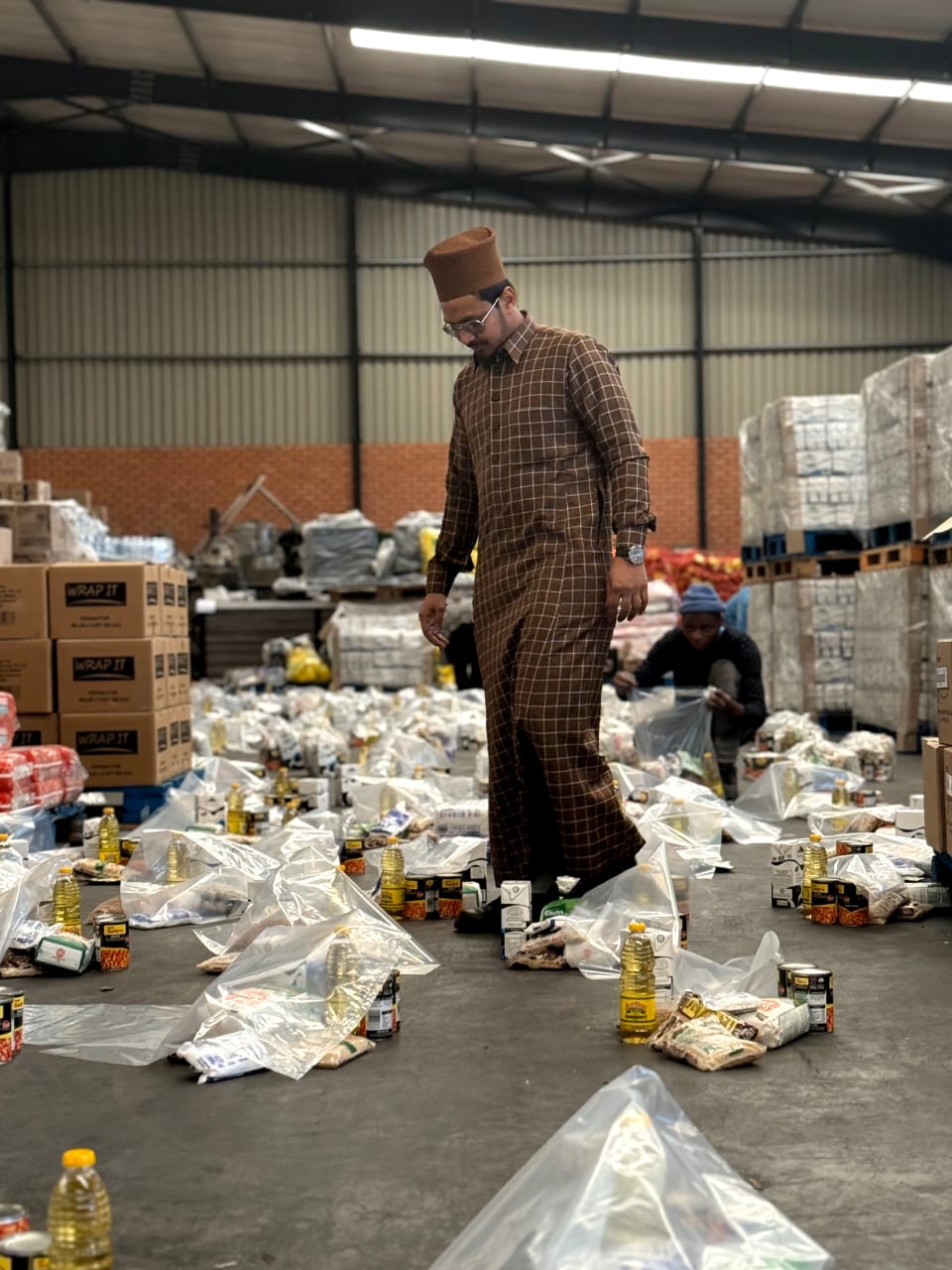 Picture showing the Director of Al-Hashmi Institute walking between food hampers to be distributed to the poor.